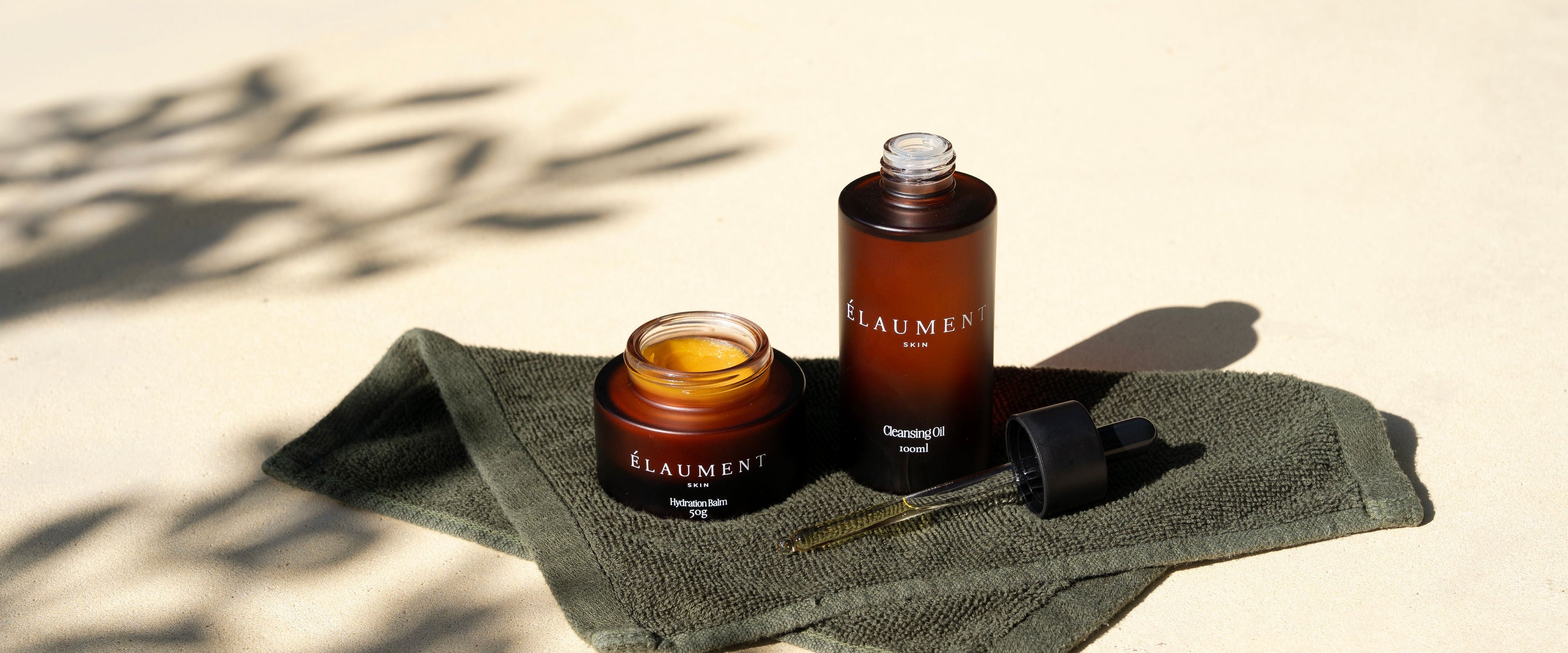 Élaument Skin Cleansing Oil and Hydration Balm on an olive washcloth in sunlight
