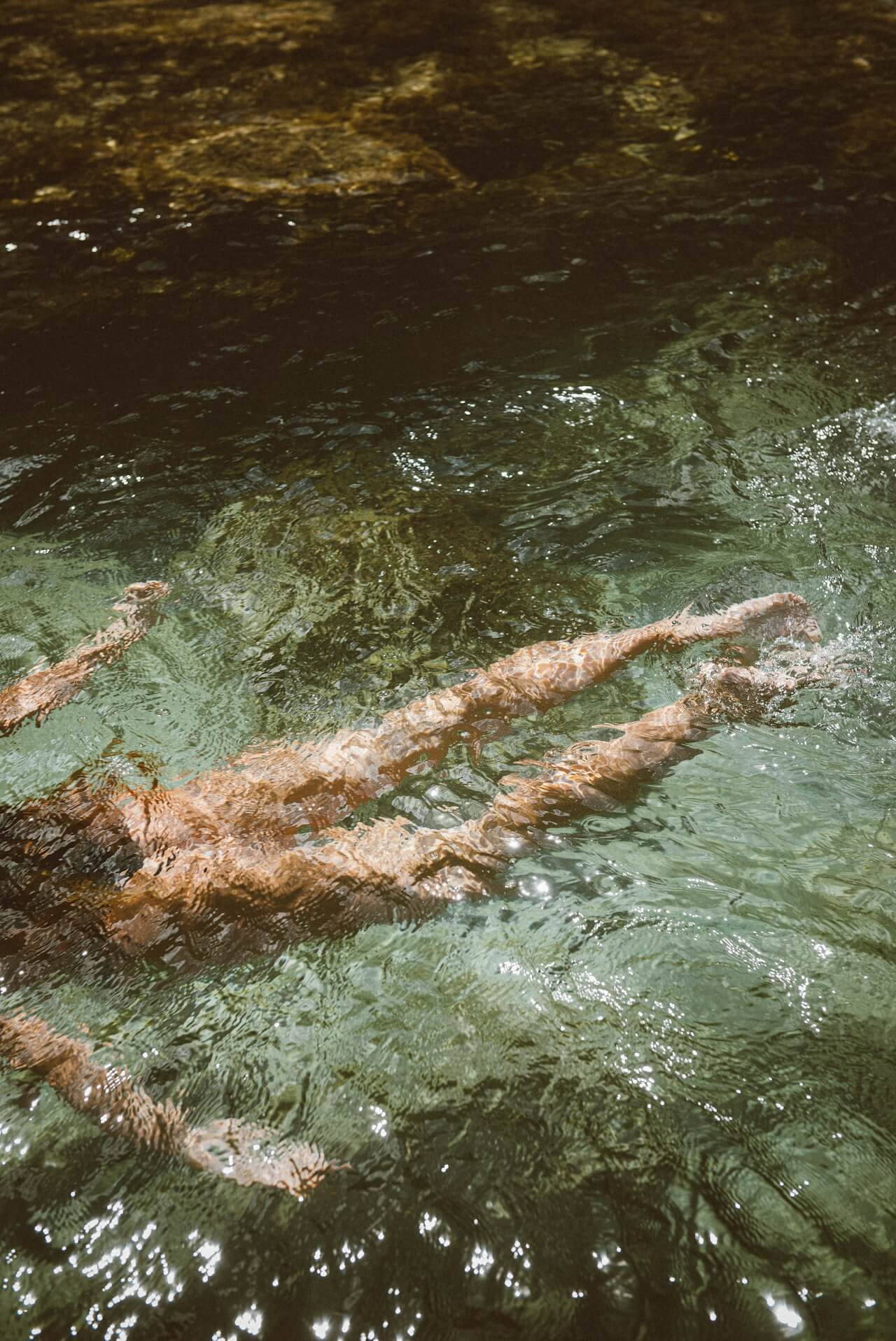 Person swimming in a natural body of water with greenish hue