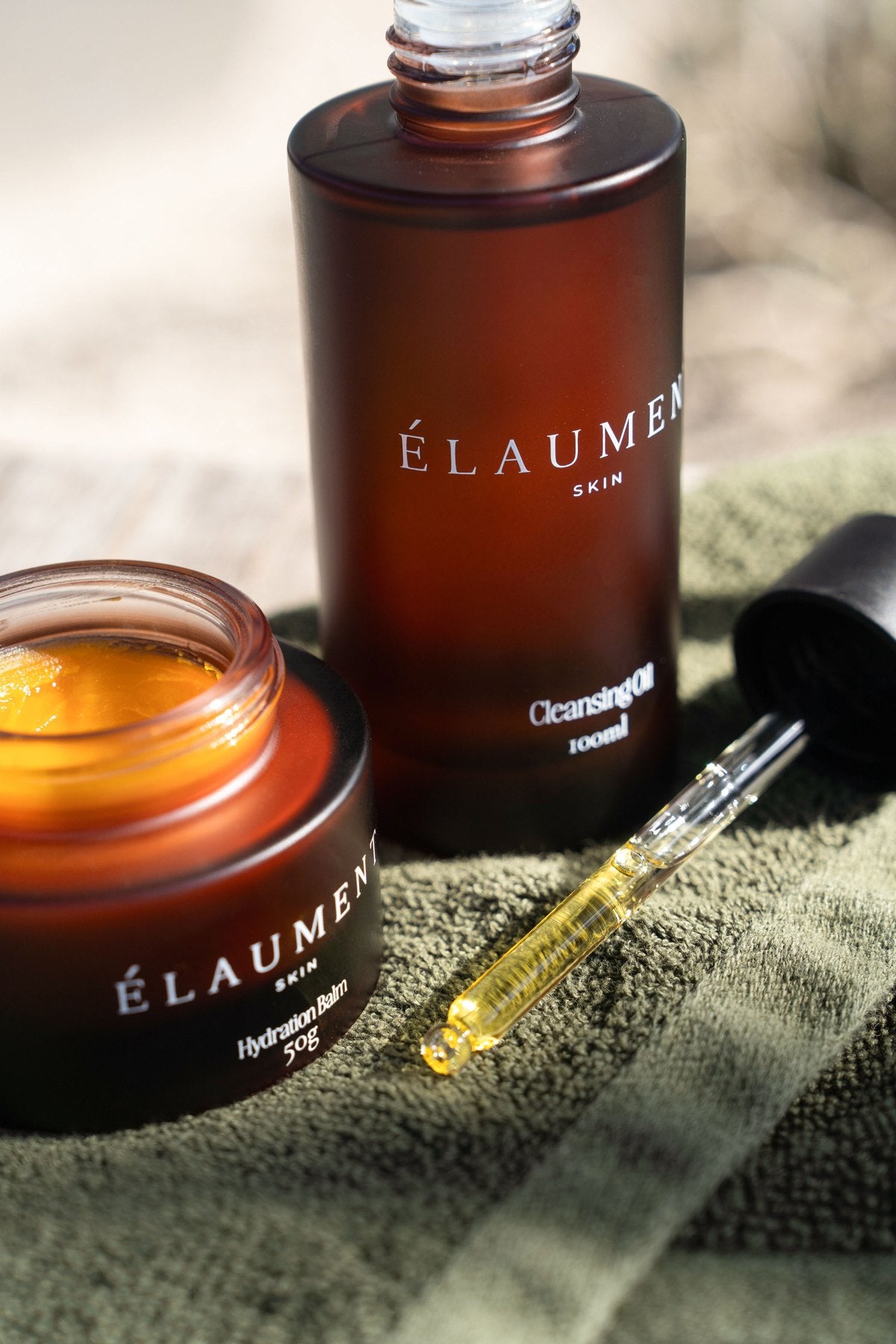 The Élaument Cleansing Oil and Hydration Balm on an olive washcloth